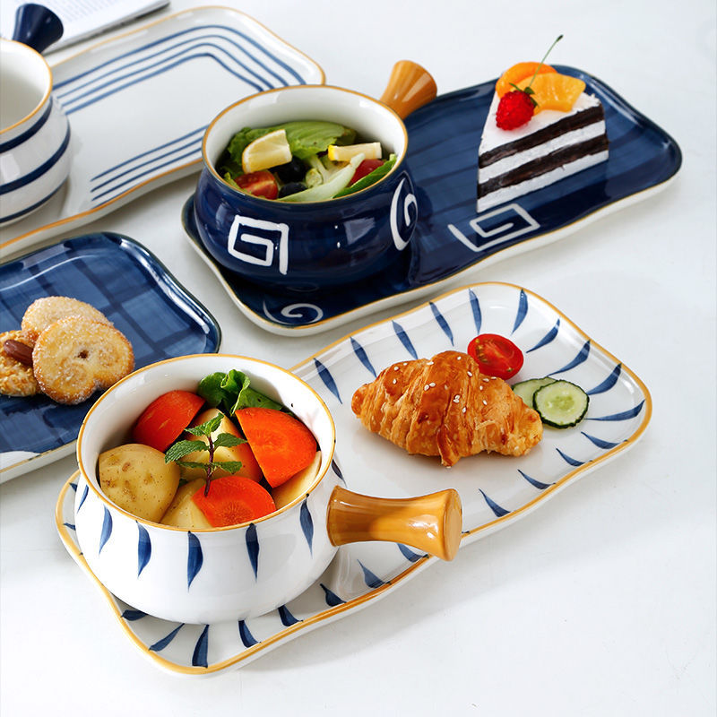 Assorted food items on decorative plates with a focus on a bowl of salad and a croissant.